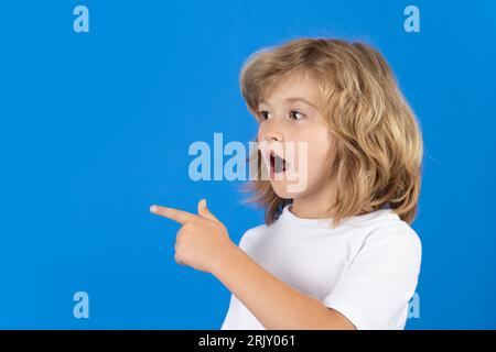 Surprised child looking away, pointing finger on isolated studio background. Shocked kid pointing to copyspace, showing promo offers, points away Stock Photo