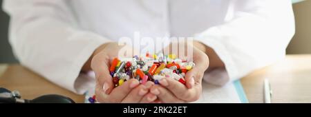 Doctor with stethoscope holds bunch of multi-colored pills in her hands close up. Stock Photo