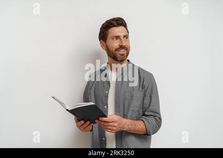 Smiling man in casual clothes standing with open notepad and looking at side white background Stock Photo