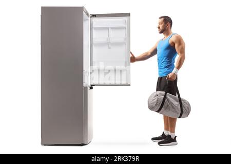 Fit man holding a sports bag and opening an empty fridge isolated on white background Stock Photo