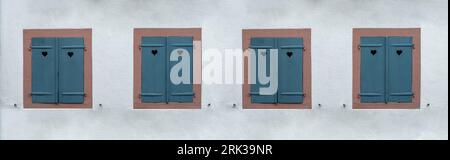 Windows with blue closed wooden shutters on white stone wall background. Shutter with heart hole, love symbol. Stock Photo