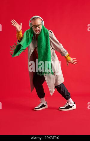 Full-length photo of positive, funny elderly man with beard in bright, stylish outfit with headphones who dancing with happiness. Stock Photo