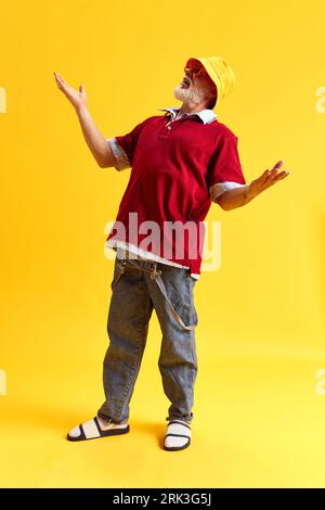 Full length portrait of attractive cheerful funny man staying with raising hands and smiling isolated over yellow color background Stock Photo