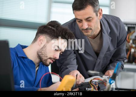 supervisor guiding apprentice using a multimeter Stock Photo