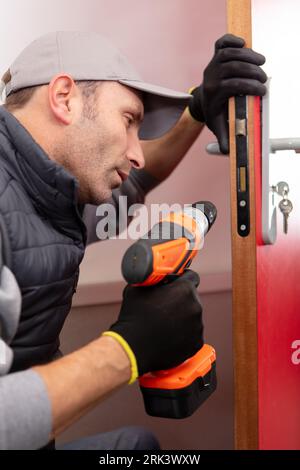 young contractor using cordless drill on door lock Stock Photo