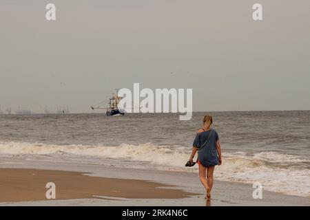 Walking on the beach while fishing boat sails nearby Stock Photo