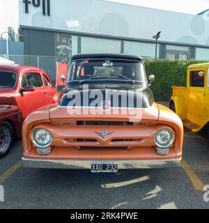 An old black and orange 1956 Ford F 100 V8 pickup truck in a parking lot at a classic car show Stock Photo