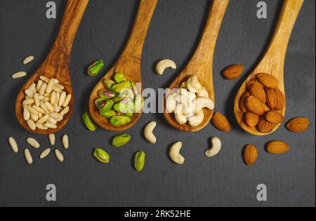 Nuts mix with pine nuts, pistachios, cashews nuts and almonds in wooden spoons top view closeup on dark gray background. Stock Photo