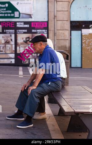Pamplona, Spain - July, 31: An old man wearing a blue shirt sitting on a bench in the streets of Pamplona Stock Photo