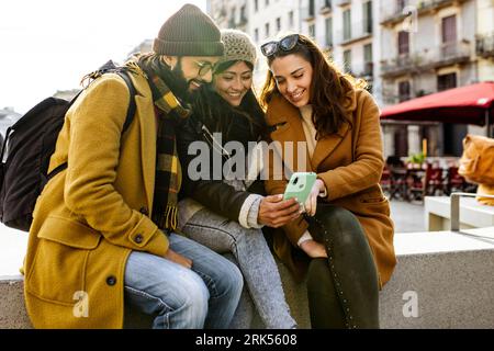 three happy friends using mobile phone on the street at winter. Group of students having fun outside Stock Photo