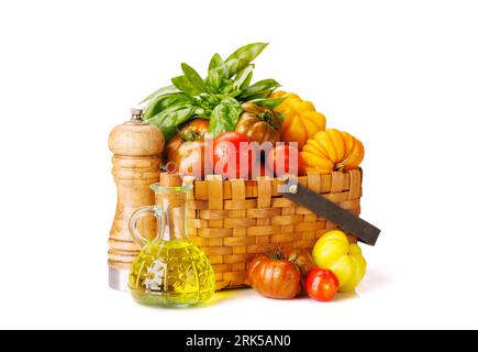 Assorted tomatoes in rustic basket, garden basil and spices. Isolated on white background Stock Photo