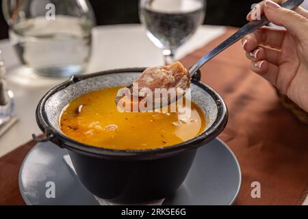 Kidney beans soup with smoked ham in small cauldron on the restaurant table Stock Photo