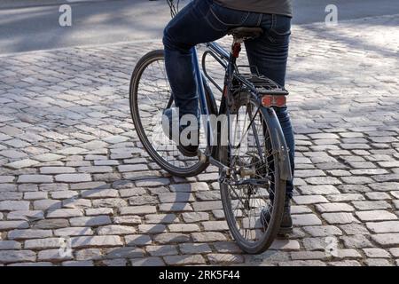 man with black city bike stands on cobblestones Stock Photo