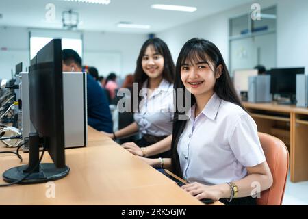 Two Asian female students smiling and looking at the camera while sitting in a classroom setting Stock Photo