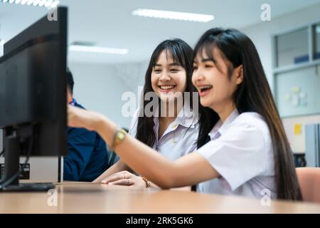 Two Asian female students smiling while pointing at a computer screen Stock Photo