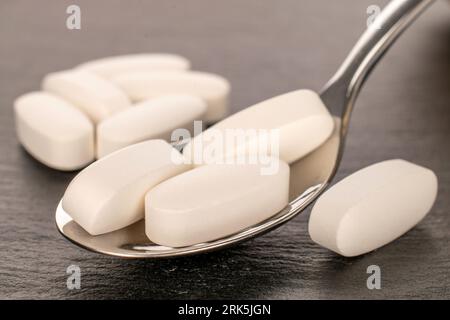 Several medical pills with metal spoon on slate stone, macro. Stock Photo