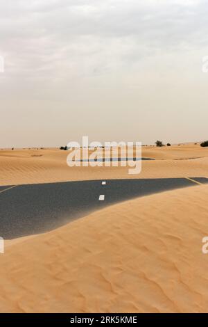 (Selective focus) Stunning view of a deserted road covered by sand dunes. Empty road that run through the Dubai desert. Dubai, United Arab Emirates. Stock Photo