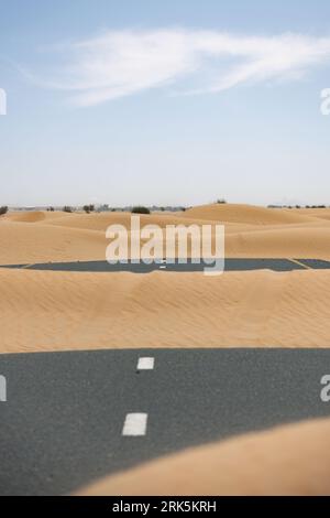 (Selective focus) Stunning view of a deserted road covered by sand dunes. Empty road that run through the Dubai desert. Dubai, United Arab Emirates. Stock Photo