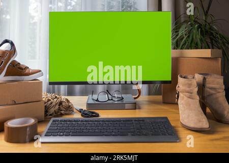 online footwear store mockup, computer monitor with blank green screen on the desk at home. SME business Stock Photo
