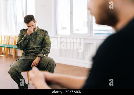 Portrait of group male soldiers in camouflage uniform talking sitting in circle during PTSD group therapy session. Concept of mental health Stock Photo