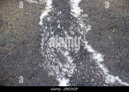 white soapy foam in gray dirty water in a puddle on the ground outside Stock Photo