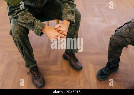 Closeup high-angle view hands of unrecognizable veteran male in camouflage uniform with disability attending PTSD support group speaking about his Stock Photo