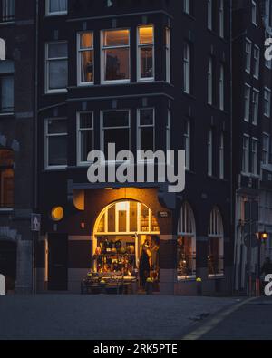 The warm light of a shop in Amsterdam contrasts against the cool blue hues of early evening. Stock Photo