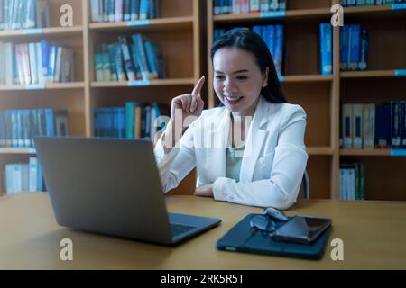 A woman sitting in a library during an online lecture Stock Photo