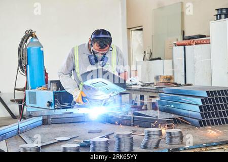 working man in a workshop/factory. man working on metal. metalworking. iron welding and using industrial equipment Stock Photo