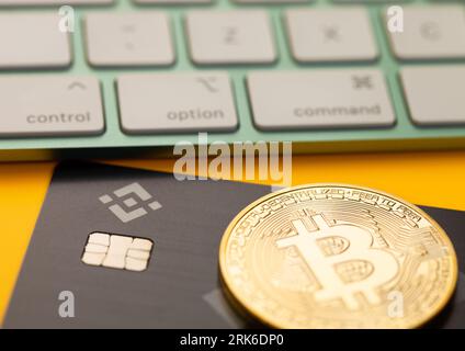 LONDON,UK - NOVEMBER 16, 2022: Binance credit card with two bitcoins and keyboard for cryptocurrency trading market on yellow background. Macro Stock Photo
