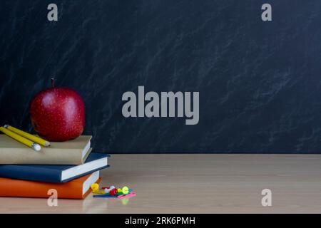 A stack of books, one red apple and colorful, school supplies, on a black  background of the blackboard with a place for the inscription. Stock Photo