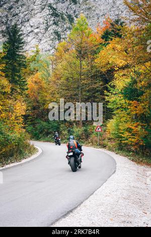 Motorcyclists ride on the road through the autumn forest in the mountains. Stock Photo