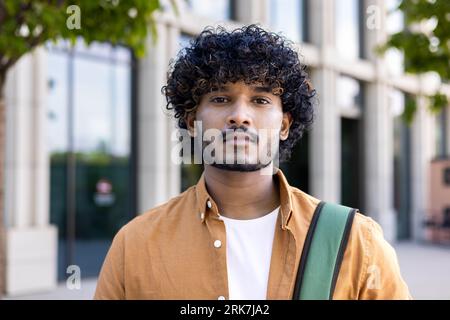 Close-up photo. Portrait of a young Indian male programmer, developer standing on the street and confidently and seriously looking at the camera. Stock Photo