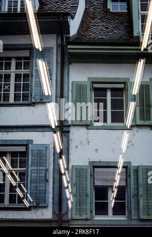 Architectural detail of historical houses seen through a glass window with neon lights reflected on it, Basel, Switzerland Stock Photo