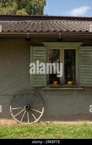 Picturesque garden shed or small cottage with old variate wheel leaning against the wall and window shutters open Stock Photo