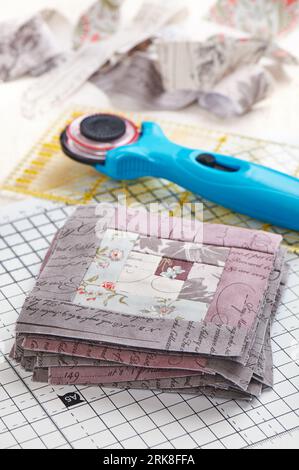 Patchwork log cabin blocks on craft mat, stack of blocks, sewing accessories on white wooden surface Stock Photo