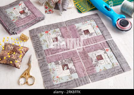 Patchwork log cabin blocks, stack of blocks, sewing accessories on white wooden surface Stock Photo