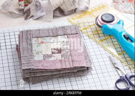 Patchwork log cabin blocks on craft mat, stack of blocks, sewing accessories on white wooden surface Stock Photo