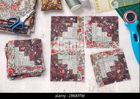 Patchwork log cabin blocks, stack of blocks, sewing accessories on white wooden surface Stock Photo