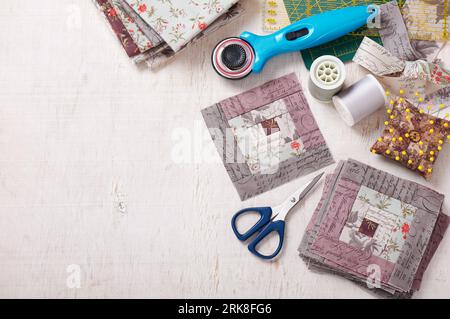 Patchwork log cabin blocks, stack of blocks, sewing accessories on white wooden surface Stock Photo