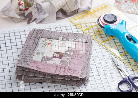 Patchwork log cabin blocks on craft mat, stack of blocks, sewing accessories on white wooden surface Stock Photo
