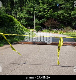 Telephone Pole with wires still attached lies across a neighborhood street by blind curve with yellow caution tape stretched across the road in the fo Stock Photo