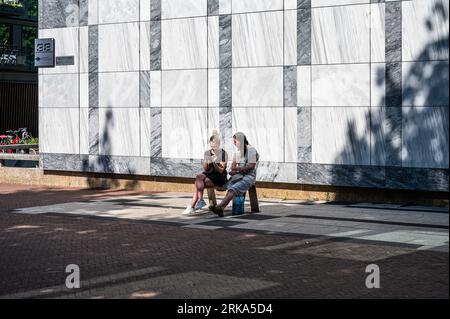 Arnhem, Gelderland, The Netherlands, 08 24 2023 - Two young woman sitting at the city hall building Stock Photo