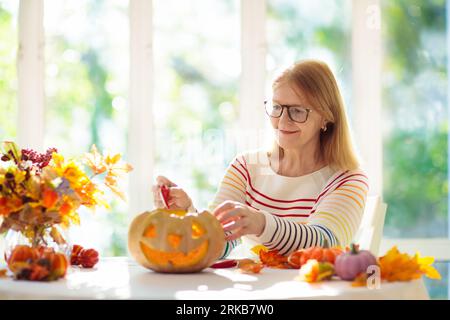 Family carving pumpkin for Halloween celebration. Woman cutting jack o lantern for traditional trick or treat decoration. Female decorate home. Stock Photo