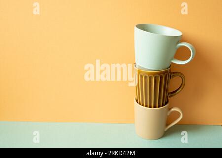 Stack of mug cup on mint green table. orange wall background. copy space Stock Photo
