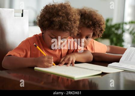 Curious boy looking how his brother writing in notebook when doing difficult assignment Stock Photo