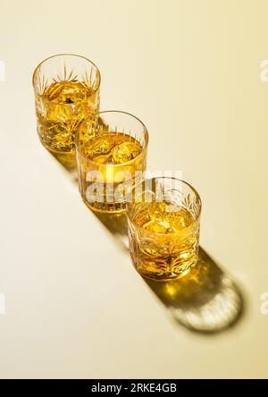 Three whiskey glasses with ice cubes on golden background. Stock Photo