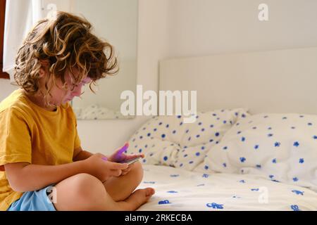 Boy with smartphone sitting on bed Stock Photo