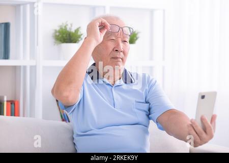 Presbyopia, senior asian man holding eyeglasses having problem with vision problem trying to read text on mobile phone Stock Photo