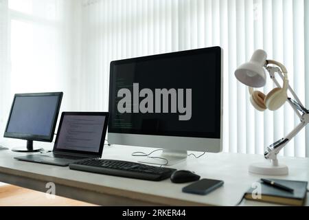 Computers and laptop with programming code on screens in office of it company Stock Photo